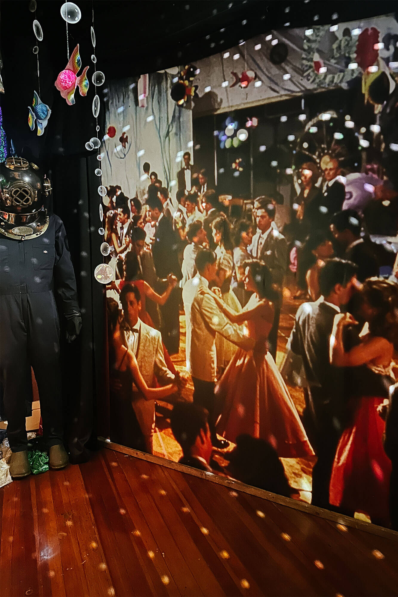 A prom-themed room featuring an enlarged print of the 'Back to the Future' dance, with an under-the-sea theme enhanced by light reflections from a disco ball, creating a playful and romantic ambiance during a couple’s stay at an Ohio adventure getaway.