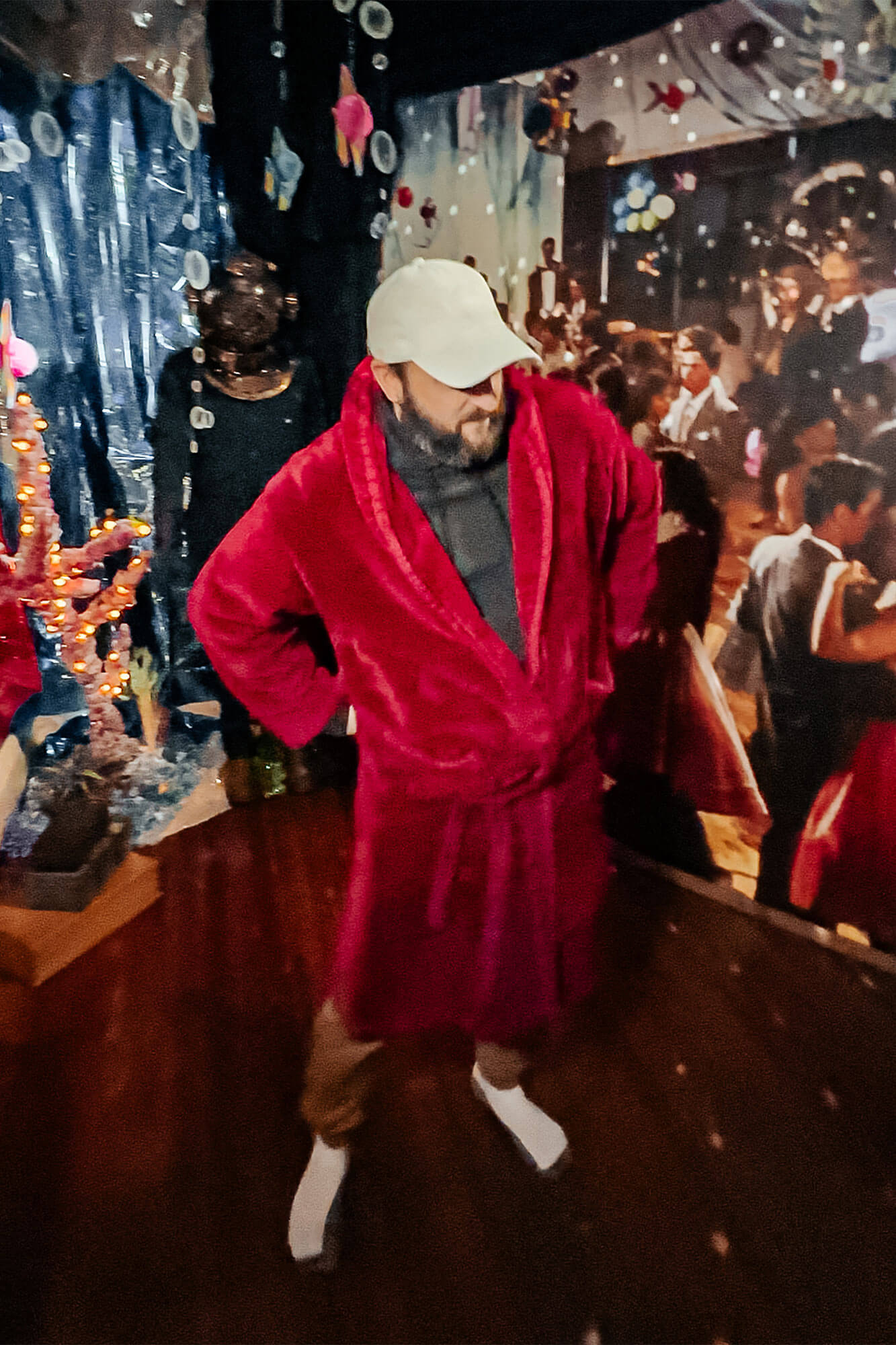 A man in a red robe standing in a prom-themed suite, complete with nostalgic elements like a Back to the Future dance print and playful disco ball lighting, part of an adventurous romantic escape in Ohio.