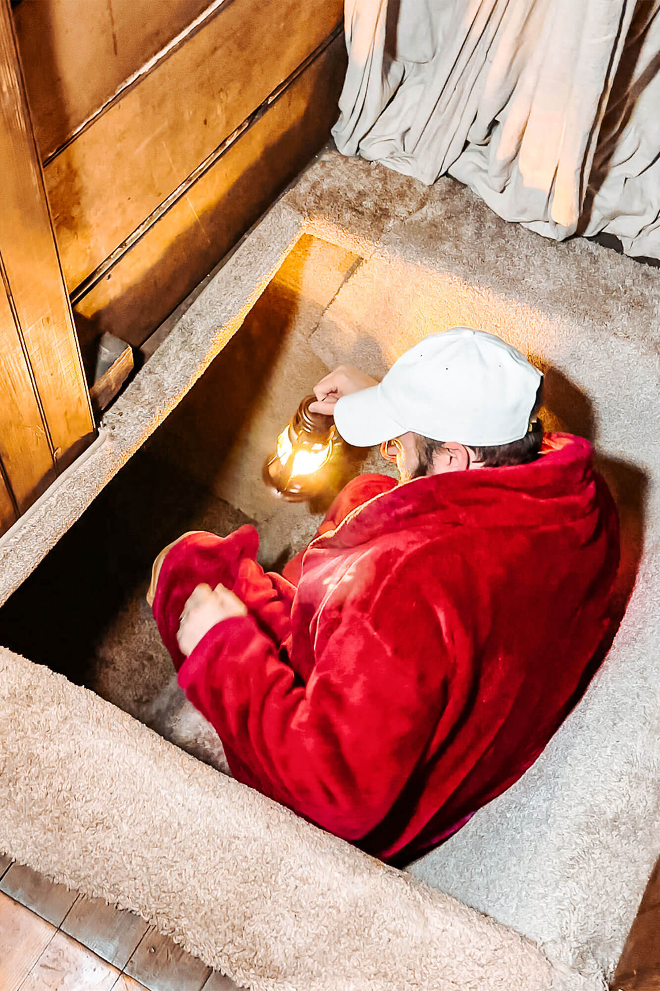A man dressed in a red robe holding a glowing lantern, crawling into a secret passage in a themed suite during a romantic Ohio getaway full of adventure and mystery.